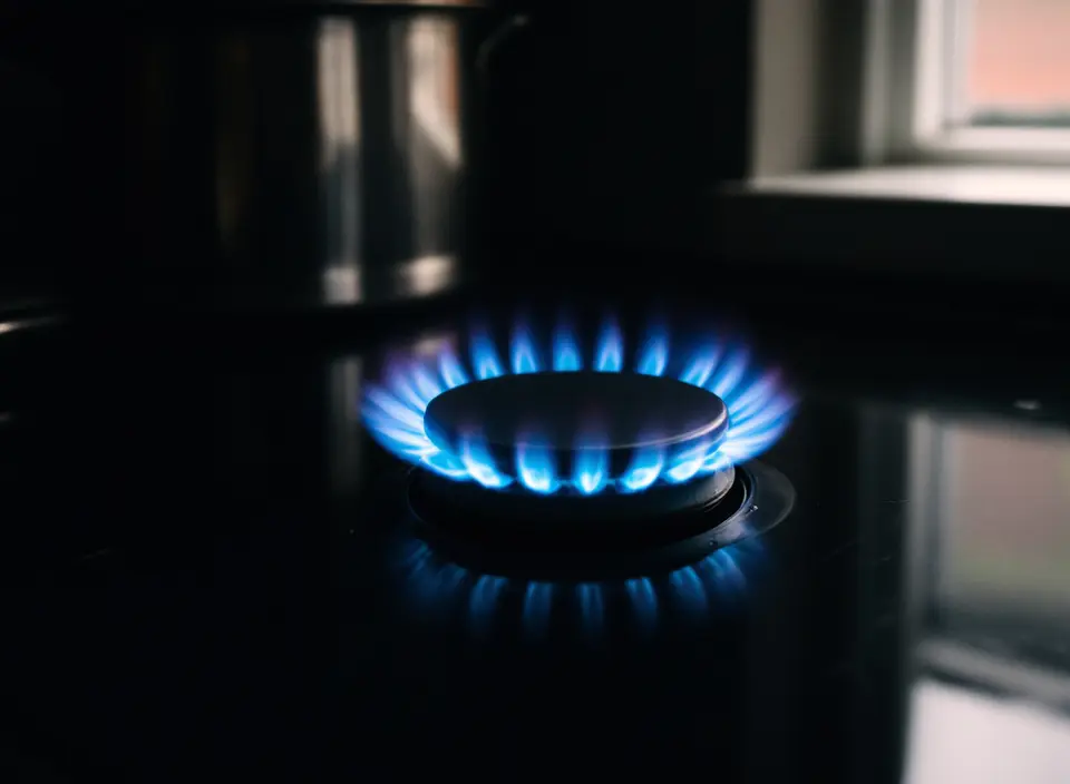 Een blauwe gasvlam op een pit van een gaskookplaat in een donkere keuken