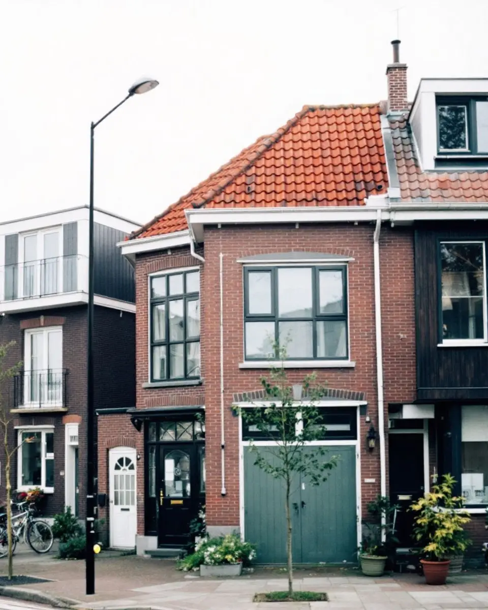 Een straathoek met verschillende woningen naast elkaar: een appartementengebouw met balkons, een bakstenen huis met rode pannen en een woning met donkere houten gevel